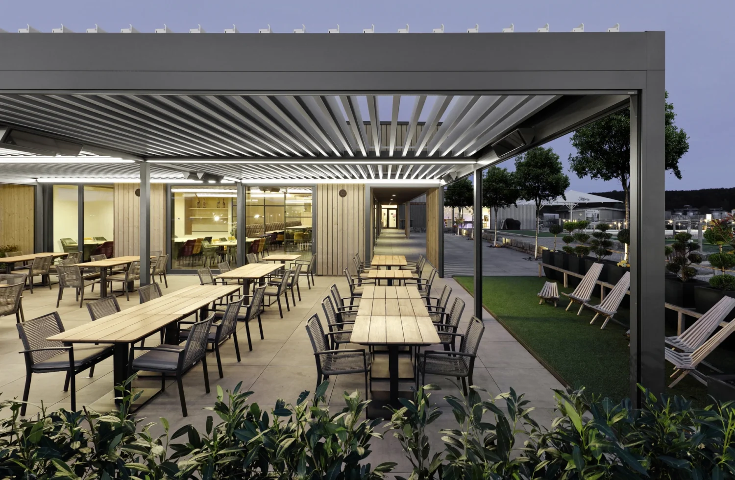 Stilvolle Außenterrasse mit Lamellendach und Beleuchtung Moderne Außenterrasse bei Abenddämmerung mit stilvollen Sitzgelegenheiten